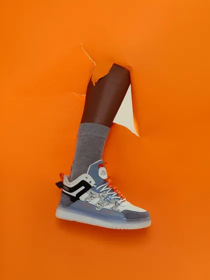 A creative and surreal shot of a leg breaking through an orange paper background. This high-concept image is designed to be disruptive and grab attention instantly in a busy feed.