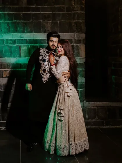 A stylish couple portrait against a brick wall, lit with green light for a modern and edgy Sangeet look.