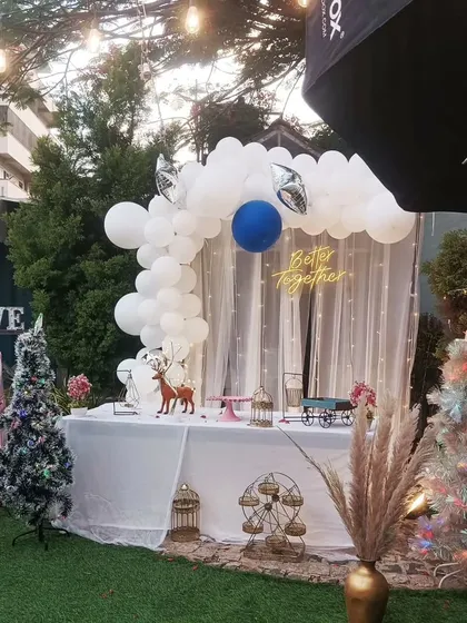 A bright and cheerful daytime party setup. A white balloon arch and a "Better Together" neon sign create a lovely photo backdrop, complemented by whimsical elements like decorative deer and Christmas trees.