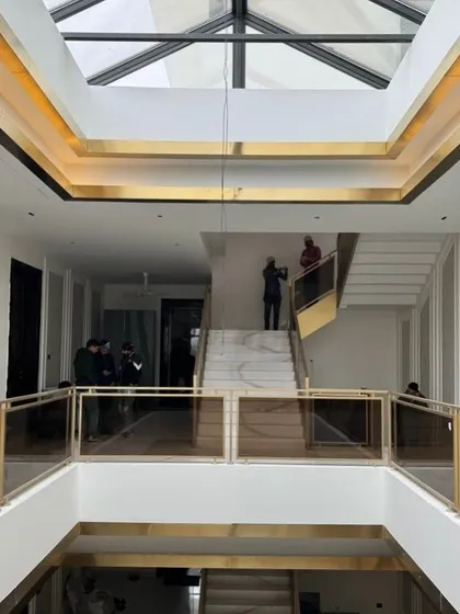 A project nearing completion. This shot captures the moment when the architectural vision comes together with the interior finishes, showing the double-height space with its marble staircase and stunning gold-trimmed railings being installed.