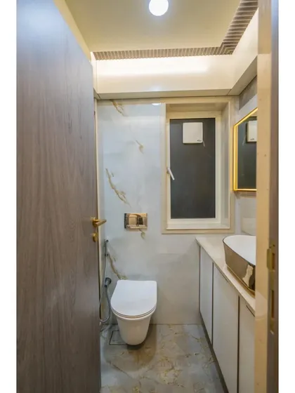 A full view of the bathroom, showing the combination of marble-patterned tiles, a modern floating toilet, and elegant gold accents.