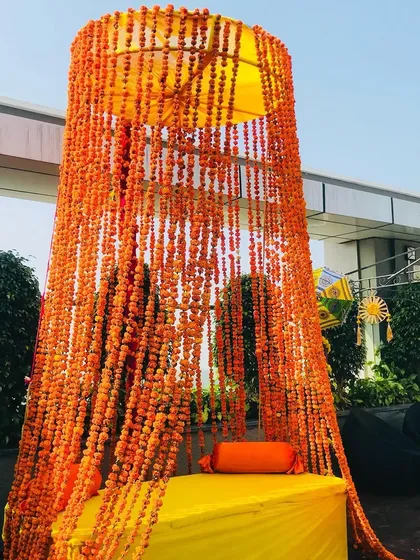 A unique seating idea for a Haldi ceremony, with a canopy made of hanging marigold strings.