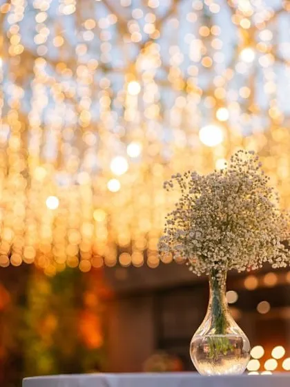 A beautiful shot focusing on a simple baby's breath centerpiece against the bokeh of the fairy light canopy.
