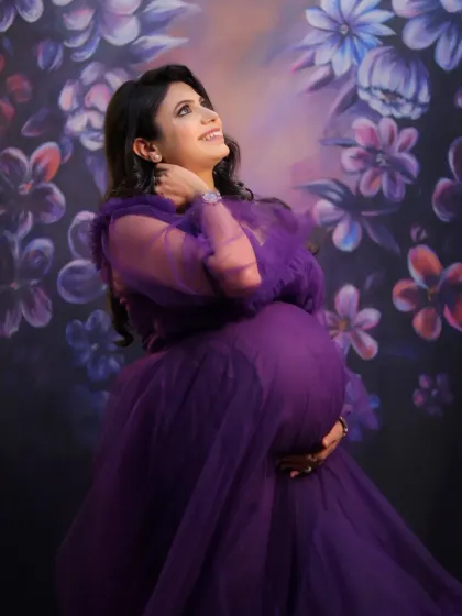A beautiful studio portrait with the mother-to-be in a purple tulle gown, looking up joyfully against a painted floral backdrop.