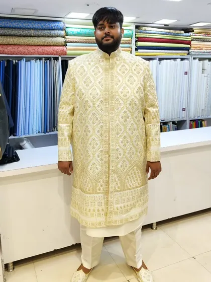A client looking pleased in his custom-fit, heavily embroidered gold and white sherwani. This outfit is designed to make you feel like royalty on your big day.