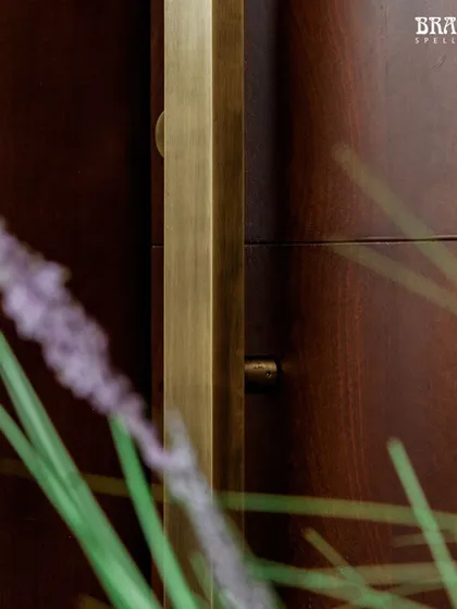 A detail shot of the 10-foot handle's surface. The Antique Brass Matte finish gives it a subtle, warm glow that catches the light beautifully, adding texture and depth to the minimalist door design.