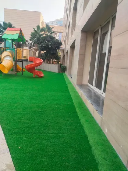 A side view of the same children's play area, showing how the artificial grass provides a clean, neat edge against the building's foundation.