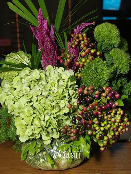 A smaller floral arrangement featuring green hydrangeas, purple berries, and other unique botanicals.