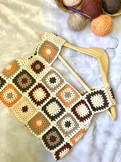 My crochet crop top laid out on a hanger, showing the full pattern. Each square is a mini work of art, coming together to create a unique garment.