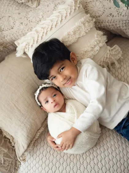 An adorable overhead shot of a big brother cuddling his newborn sister. She looks right at the camera, making for a precious and engaging portrait.