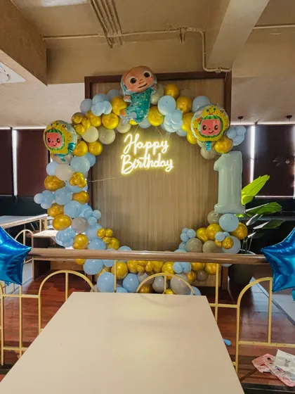 A Cocomelon-themed first birthday party. This popular theme includes a circular balloon arch, a 'Happy Birthday' neon sign, and Cocomelon character foil balloons.