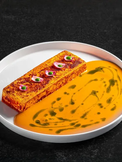 A unique presentation of a paneer dish, served as a block in a pool of tomato gravy with artistic drizzles.