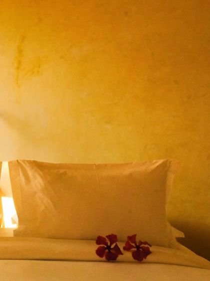 The soft texture of the pillows and the simple floral welcome detail against the warm ochre wall.