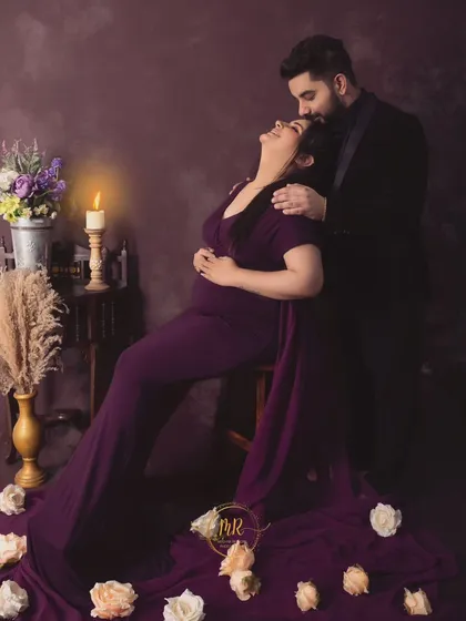 A romantic, candlelit portrait of a couple. The partner kisses his wife's forehead as she leans back, surrounded by soft light and scattered rose petals.