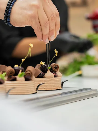 Intricate chocolate work and cherry garnishes being applied to a petit gateau by Chef Bachour.