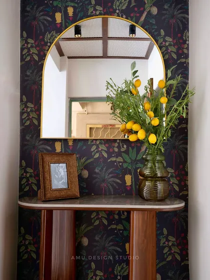 A close-up of the foyer console table against a dark, tropical wallpaper, accessorized with a gold-framed mirror and fresh flowers.