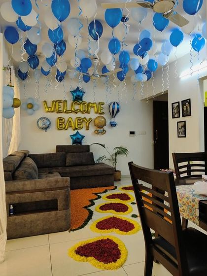 A full room view of a "Welcome Baby" home decoration. The ceiling is covered with blue and white balloons, and the floor is decorated with a pathway of flower petals.