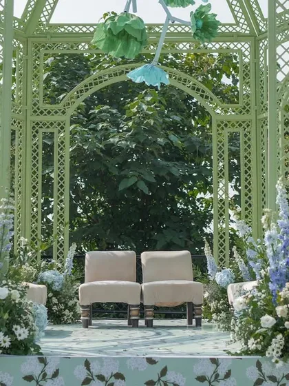 The couple's seating inside the mandap, surrounded by lush arrangements of blue and white flowers, creating an intimate and beautiful ceremony space.