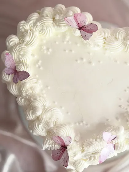 A top-down view of the heart-shaped cake, showing the delicate piping and butterfly details.