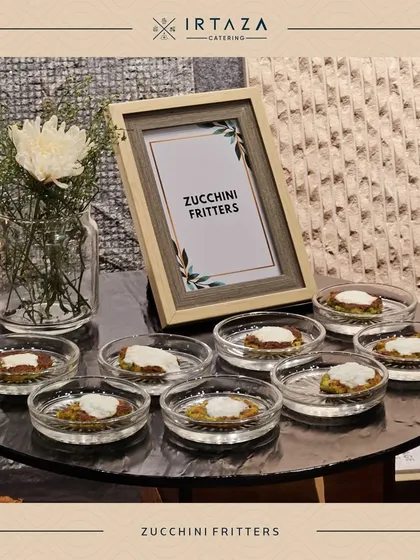 Zucchini Fritters served in individual glass dishes with a dollop of cream. This is a light and savory option, beautifully presented for a sophisticated palate.