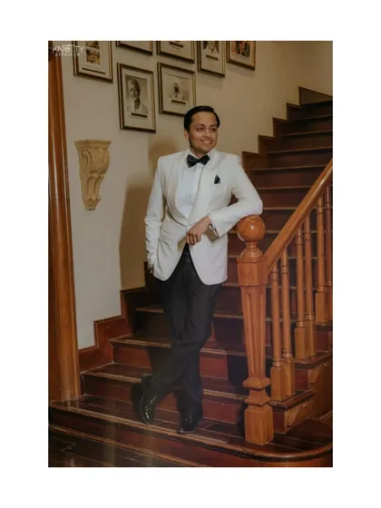 A classic portrait of the groom looking dapper in his white tuxedo and bow tie. This shot captures a moment of calm and confidence before the Sangeet night's festivities begin.