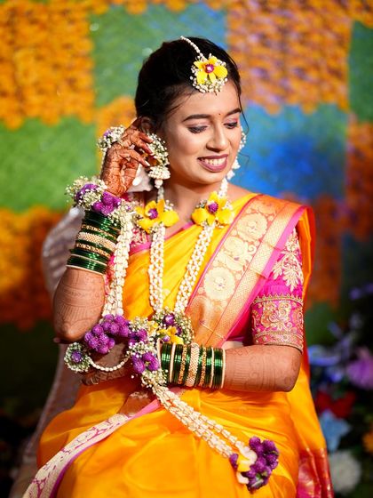A smiling Haldi bride in a bright yellow saree. Her hair is styled in a simple updo, beautifully complemented by her fresh floral jewelry.
