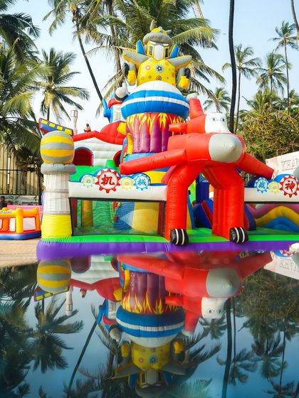 A large, robot-themed inflatable bouncy castle with a slide, perfectly reflected in the pool for a stunning visual at a waterside party.