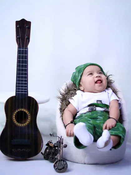 A two-month-old baby boy having a happy moment during his studio session, sitting next to a miniature guitar.