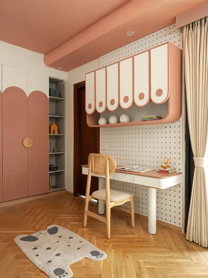 Functionality and fun coexist beautifully in this child's room. A dedicated study nook with a playful pegboard wall is paired with custom scalloped wardrobes, all tied together in a soft blush palette that feels both organized and inspiring.