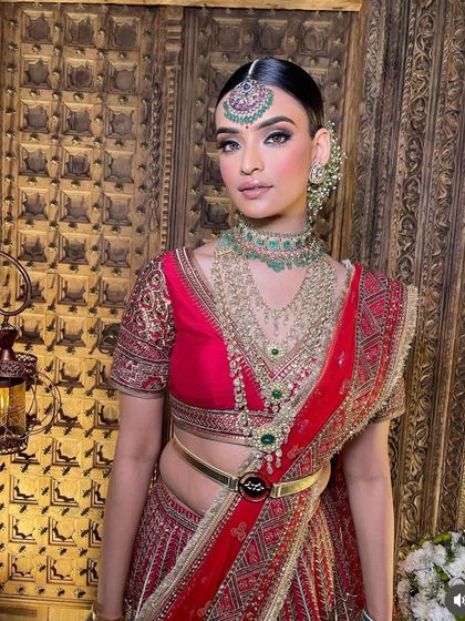A three-quarter view of the red and green bridal look, showcasing the beautiful drape of the saree and the way the makeup enhances the bride's regal posture.