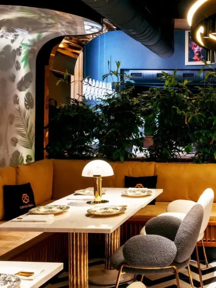 A close-up of a cozy dining nook with plush, mustard-colored banquette seating and bouclé chairs. The custom table lamp and gold-legged table add a touch of mid-century modern elegance.