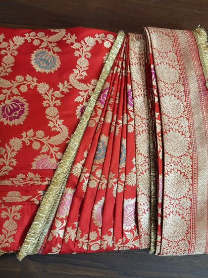 A top-down view of a box-folded red bridal saree. You can see how the pleats and the pallu are arranged to prevent wrinkles and make draping quick and easy.