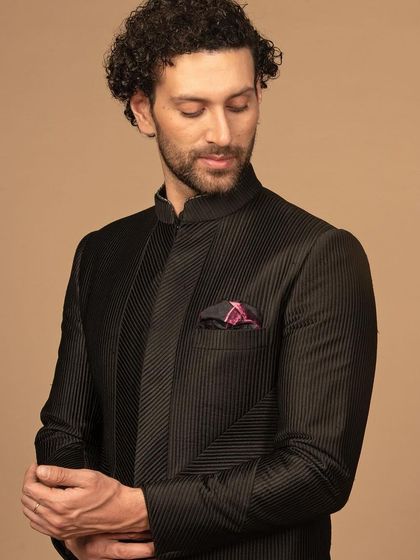 A detailed view of the black textured bandhgala, showing the quality of the fabric and the precision of the diagonal weave pattern. The patterned pocket square adds a pop of color and personality.