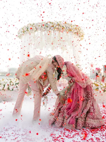 A bow of respect and love. The entire scene is enveloped in a soft, dreamy haze, with the pastel pinks of the bride's lehenga and the groom's suit creating a cohesive and romantic visual.