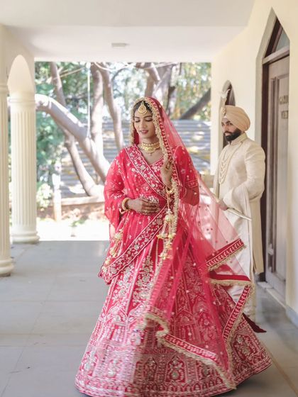 A graceful portrait of a Sikh bride in her stunning red lehenga, with her groom standing softly in the background. This shot highlights her elegance and poise.