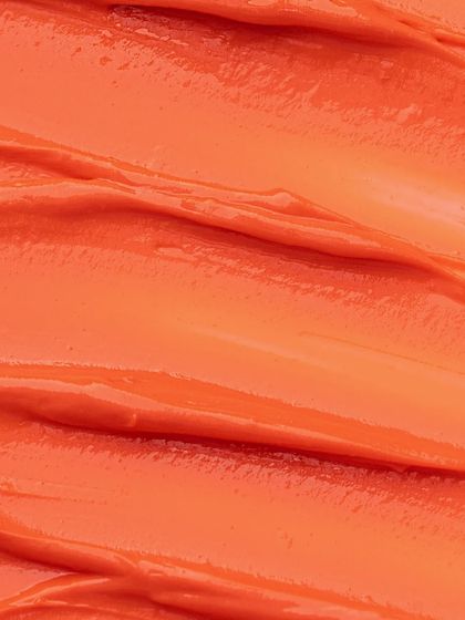 A macro texture shot of an orange cosmetic cream. These abstract, up-close shots are visually satisfying and highlight the product's color and texture.