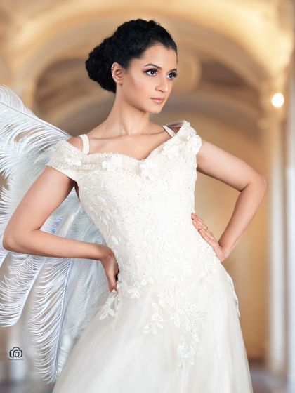 A creative portrait with the model in a white gown, with large white feathers suggesting angel wings. The background adds to the ethereal, dreamlike quality of the shot.