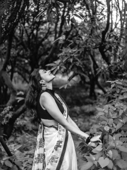 A dramatic black and white shot, capturing a free-spirited moment as the model looks up towards the sky in a lush, wooded area.