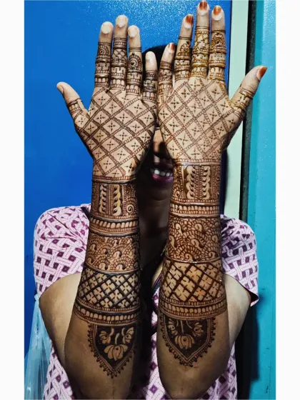 A full coverage bridal mehendi that extends up the arm. The back of the hands features a classic jaal (net) pattern, while the front includes peacocks, lotuses, and intricate bands.