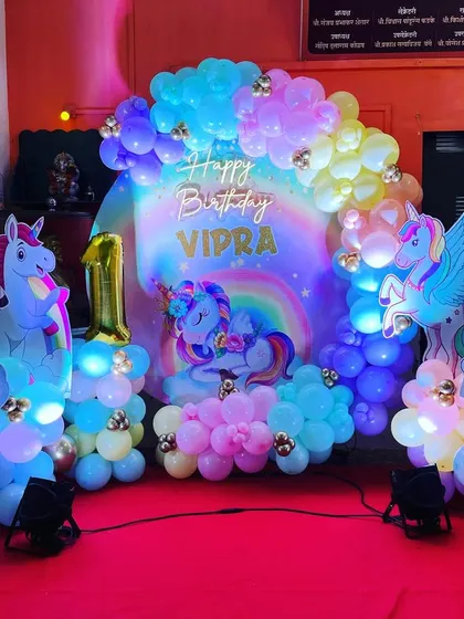 We created a magical unicorn wonderland for Vidra's first birthday. The setup glows with pastel rainbow balloons, sparkling unicorn cutouts, and a personalized neon sign, making it a truly enchanting celebration.