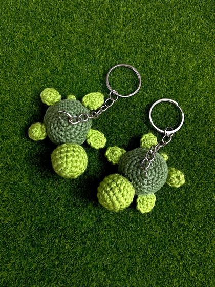 A top-down view of two of my green turtle keychains against a grassy background. The two-tone green gives them a lovely, detailed look.