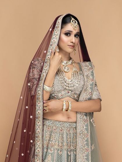 A beautifully tailored bridal lehenga with a sheer maroon dupatta. Our custom service ensures that every component of your outfit, including the draping, is designed for a flawless and elegant appearance.
