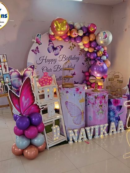 A full-stage butterfly-themed seventh birthday. The decor includes a photo collage, a 'Happy Birthday Our Beautiful Butterfly' backdrop, and a neon '7'.