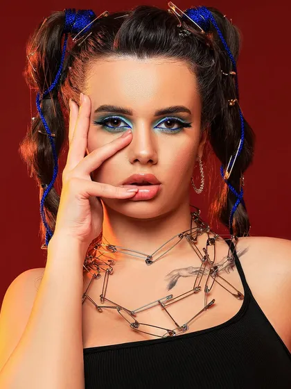 A close-up of the safety pin fashion concept, focusing on the model's expressive look and the unconventional jewelry.