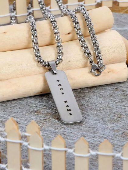 A silver-toned stainless steel pendant with a thicker, masculine chain. The engraving 'Your Name' clearly communicates the custom nature of the product.
