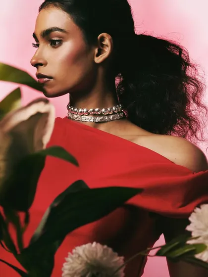 A shot for Batoki Art featuring a silver choker against a vibrant red dress. The use of foreground foliage adds depth and a sense of intimacy to this Valentine's campaign image.