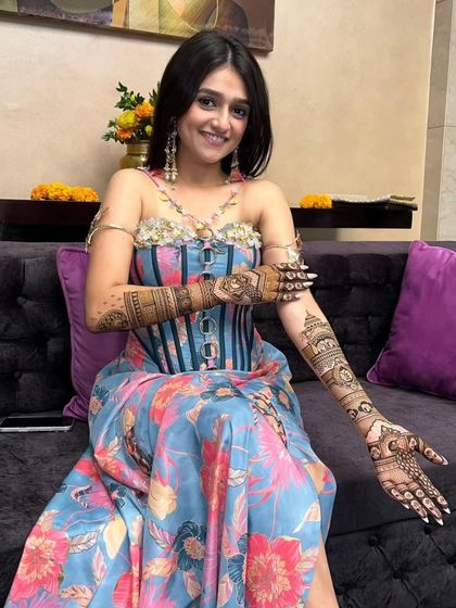 A happy bride proudly displaying her full-arm mehandi. The design is a beautiful mix of traditional and modern elements.