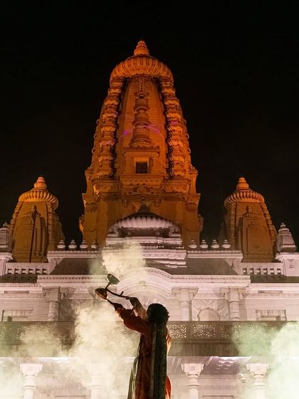 Priests performing the Maha Aarti at JK Temple in Kanpur, with smoke from the diyas creating a mystical atmosphere in front of the temple's grand facade.