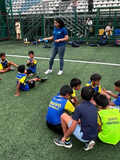 A sports psychologist engages with a small group of players sitting in a circle on the grass. These breakout sessions allow for more personalized guidance on mental conditioning.