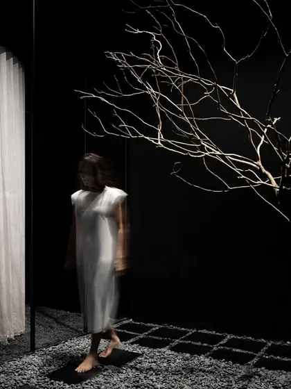 At the entrance, a bare tree stands as a sculptural sentinel. This organic element introduces a sense of stillness and natural texture into the austere, dark environment, setting a meditative tone for the retail experience that unfolds within.
